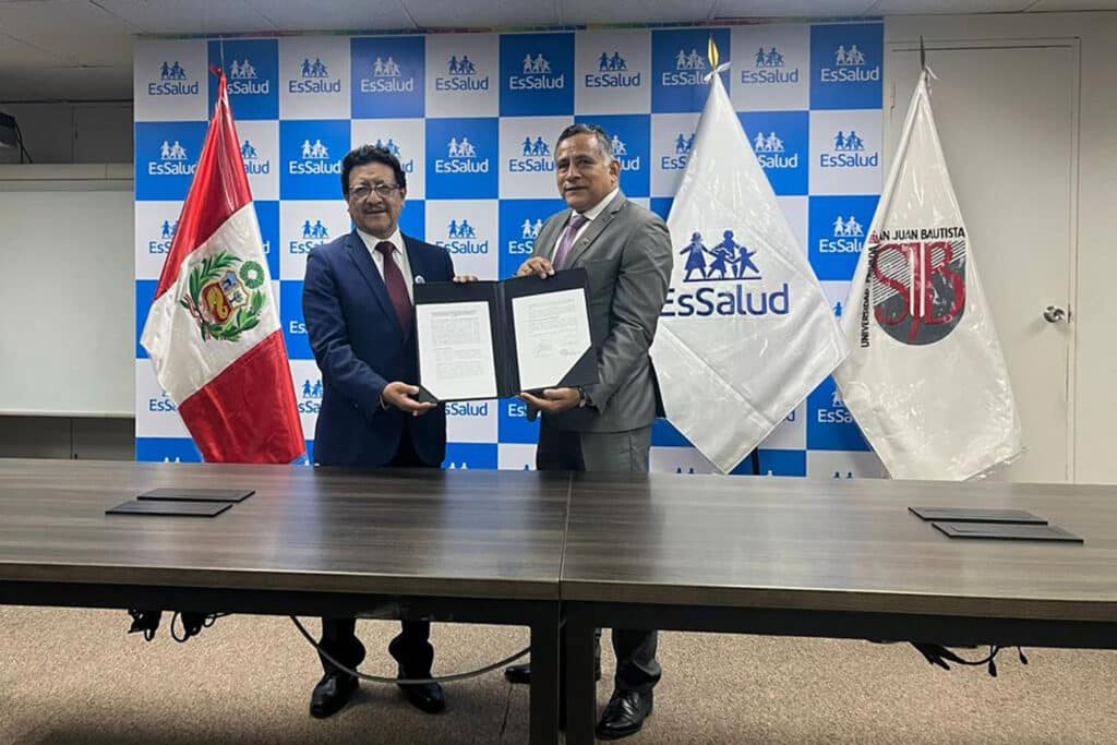 Investigación científica en salud en el Perú: Una alianza estratégica entre la UPSJB y el IETSI para el futuro médico 1 Plano medio de las autoridades de la UPSJB y EsSalud mostrando el convenio de cooperación interinstitucional firmado, de pie frente a las banderas de Perú y de la universidad.