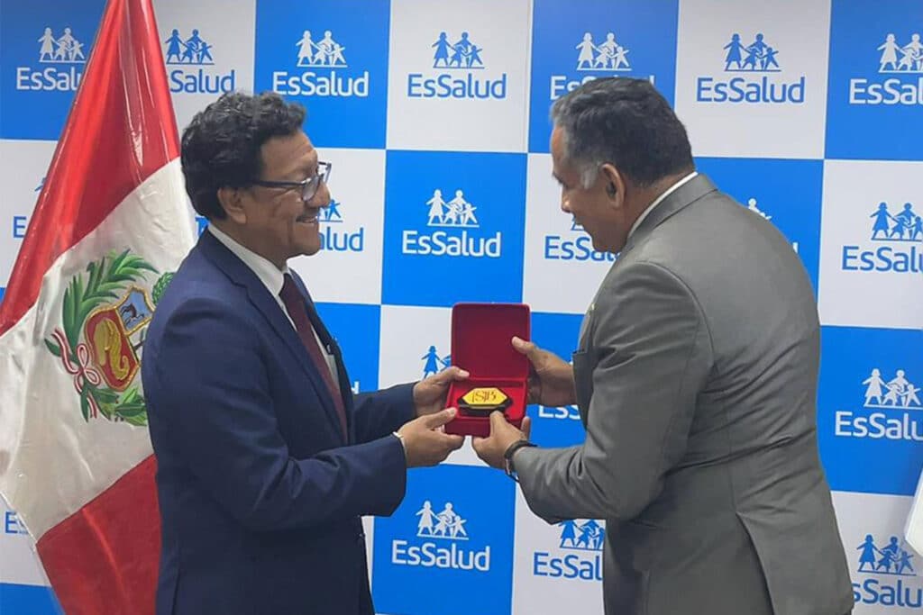 Investigación científica en salud en el Perú: Una alianza estratégica entre la UPSJB y el IETSI para el futuro médico 2 Plano de perfil del Presidente Ejecutivo de EsSalud entregando una distinción institucional en caja roja al Rector de la UPSJB en un gesto de reconocimiento durante la ceremonia de firma.