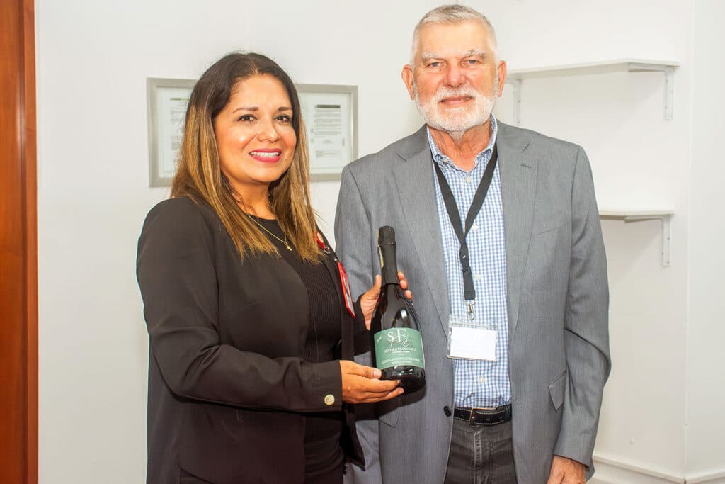 La Rectora (e) de la UPSJB, Dra. Leny Bravo Luna, y el Dr. Giorgio Milani de Italia sostienen juntos una botella de vino con una etiqueta verde de la Scuola Enologica.