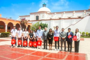 Foto grupal completa de la delegación italiana y autoridades de la UPSJB posando en el patio central del Campus Hacienda Villa, frente al edificio colonial blanco con cúpula y arcos naranjas.