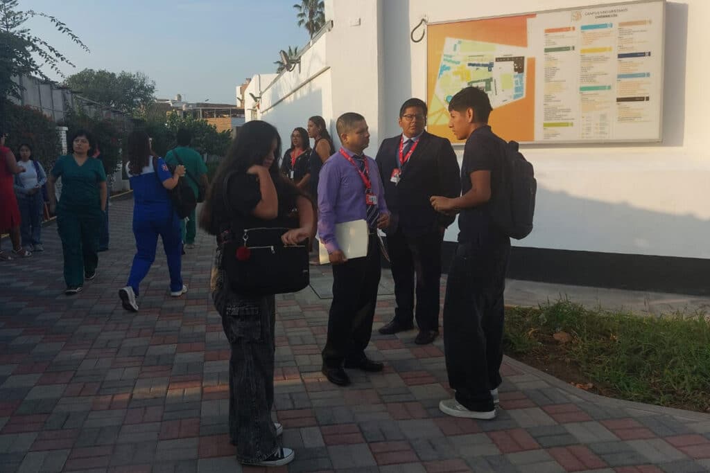 Estudiantes consultando panel informativo en campus universitario.