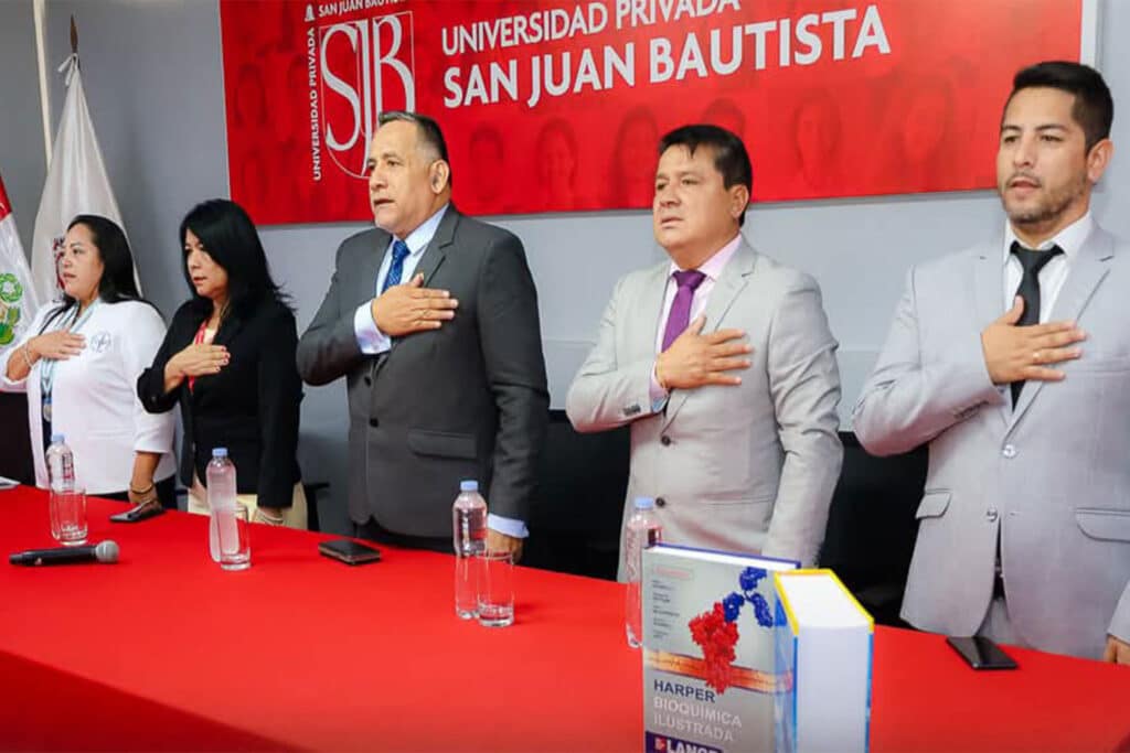 Autoridades académicas de la UPSJB de pie con la mano en el pecho durante el himno en la ceremonia de bienvenida.