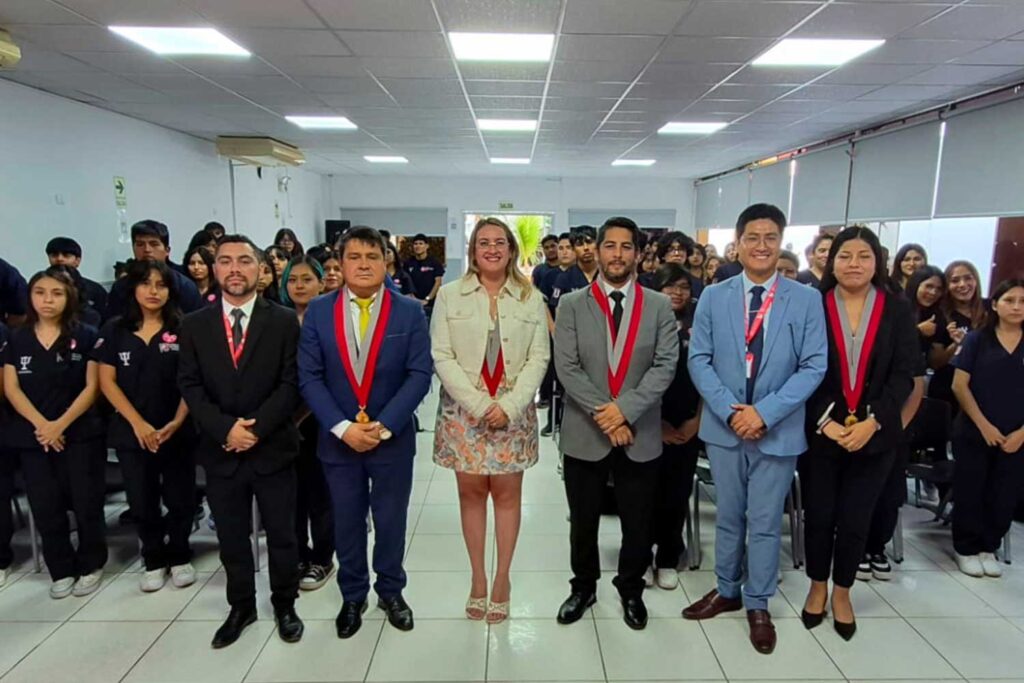 Ceremonia de Ingresantes de Psicología UPSJB: Compromiso y Vocación en Ica y Chincha 1 Un grupo grande de personas posa de pie dentro de un auditorio moderno y bien iluminado. En la primera fila, un grupo de autoridades con ropa de oficina. Detrás, una gran audiencia de estudiantes con uniformes azul marino sonríe. La sala tiene techo con paneles de luz y aire acondicionado.