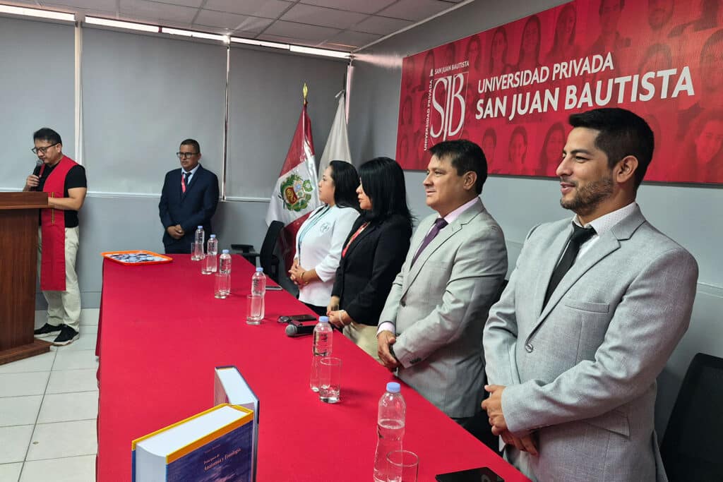 Un grupo de autoridades académicas e invitados de la Escuela Profesional de Tecnología Médica de la filial Ica de la UPSJB se encuentran de pie detrás de una mesa con mantel rojo en una sala de conferencias. Al fondo, un banner con el logo de la universidad.