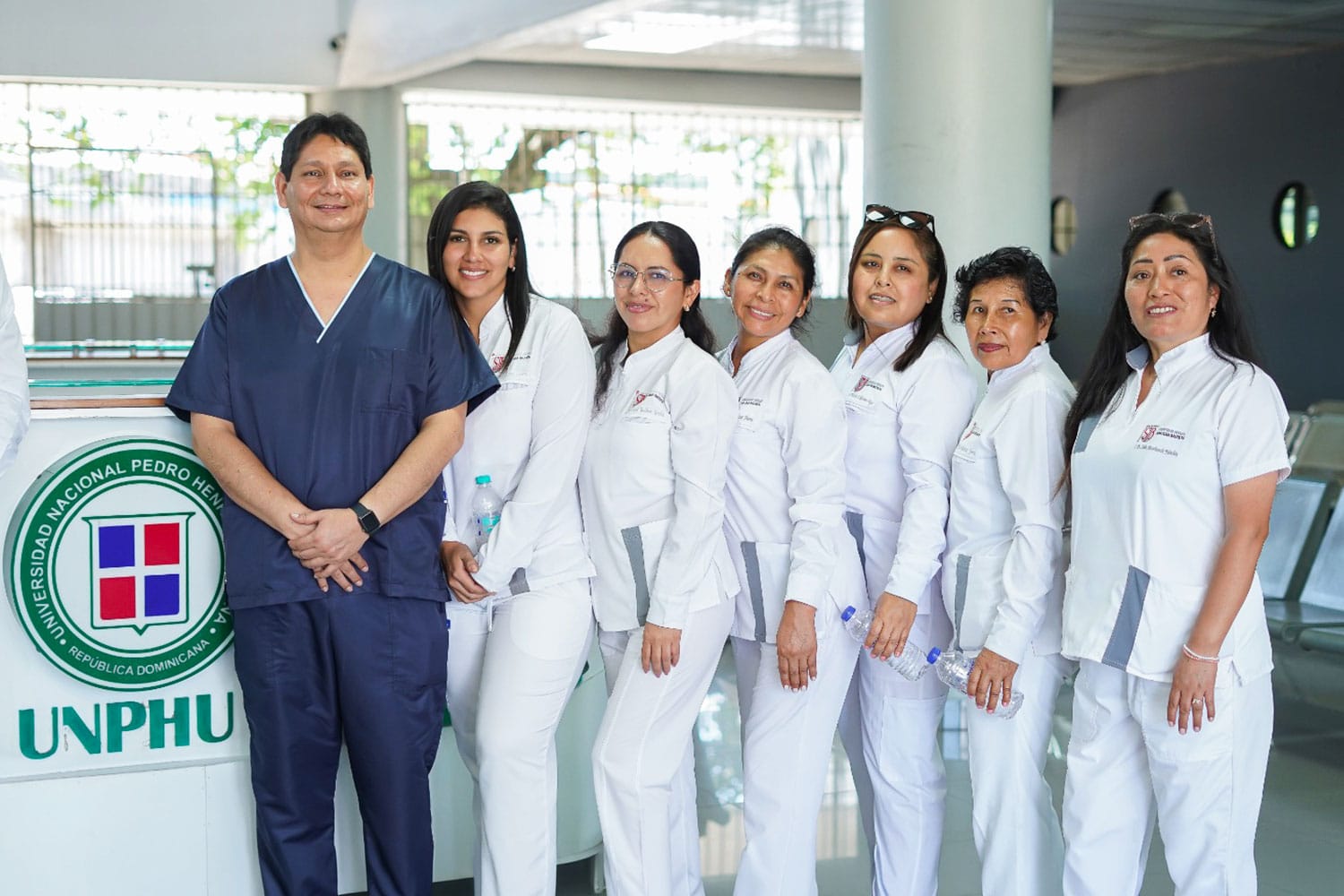 El Dr. John Paul Torres Navarro de la UPSJB junto a las residentes de la especialidad de Endodoncia posando frente al counter de recepción con el logo de la UNPHU durante la Pasantía internacional en Endodoncia.