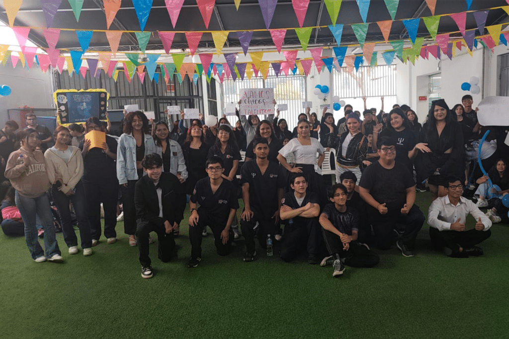 Gran grupo de estudiantes de Psicología de la sede San Borja reunidos en un patio techado decorado con banderines de colores. Algunos sostienen carteles de apoyo y motivación mientras posan sonrientes para la cámara.