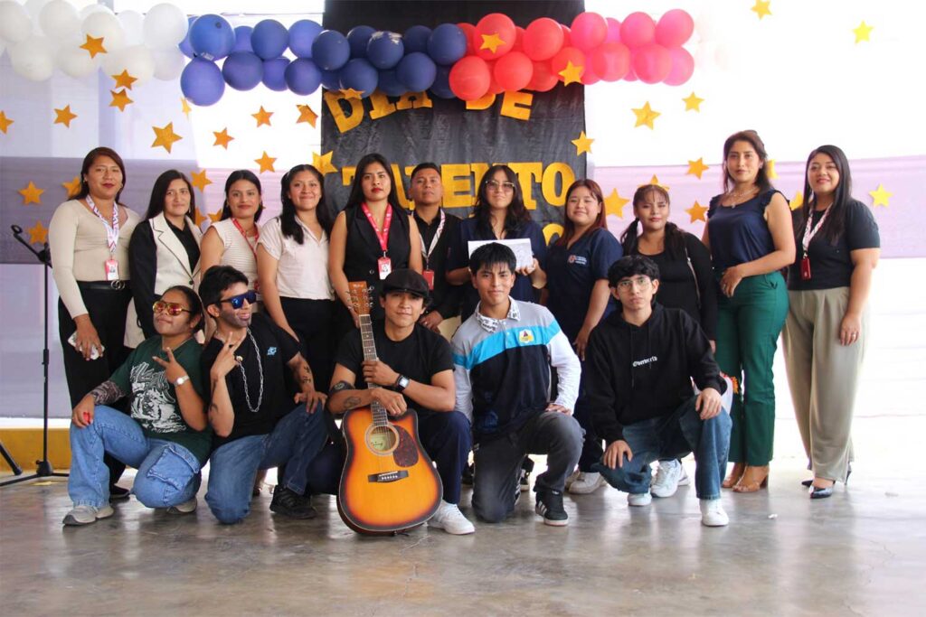 Un grupo de estudiantes de Psicología de la UPSJB filial Chincha posa frente a un mural que dice "Día de Talento". En primera fila, un estudiante sostiene una guitarra acústica rodeado de compañeros en posturas creativas.