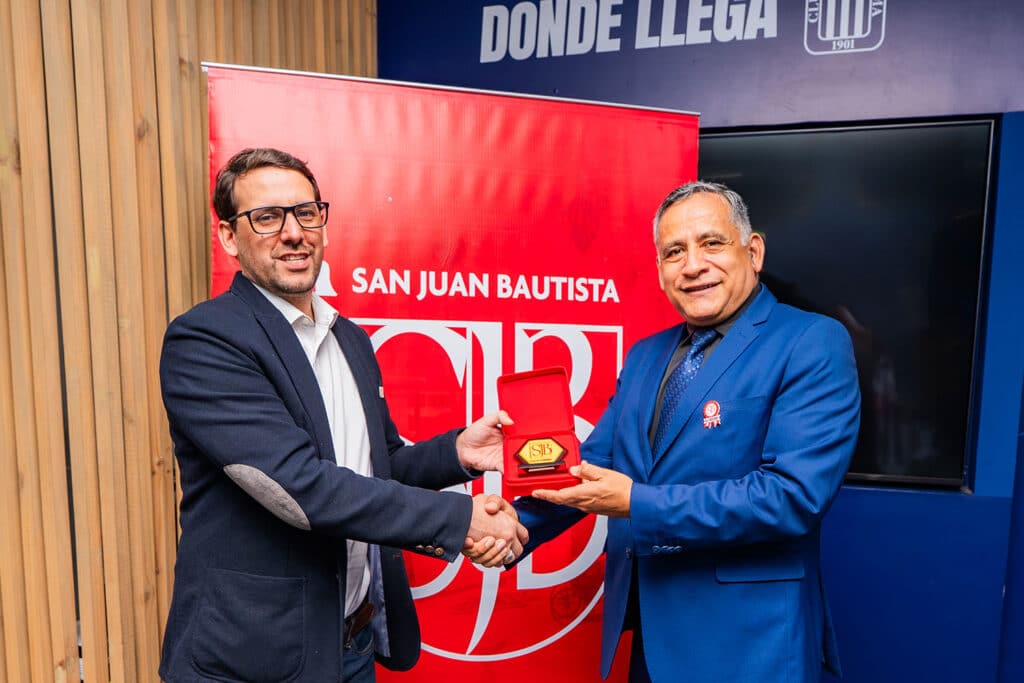 Convenio UPSJB y Alianza Lima: Colaboración estratégica por la salud y el deporte peruano 4 El rector de la Universidad Privada San Juan Bautista entrega un reconocimiento institucional al gerente de Marketing del Club Alianza Lima durante la ceremonia de suscripción del Convenio Marco de Cooperación Interinstitucional entre la UPSJB y Alianza Lima.