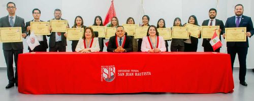 Foto grupal de autoridades de la UPSJB sentadas y un grupo de egresados de posgrado de pie mostrando sus diplomas de maestro y especialista detrás de la mesa de honor.